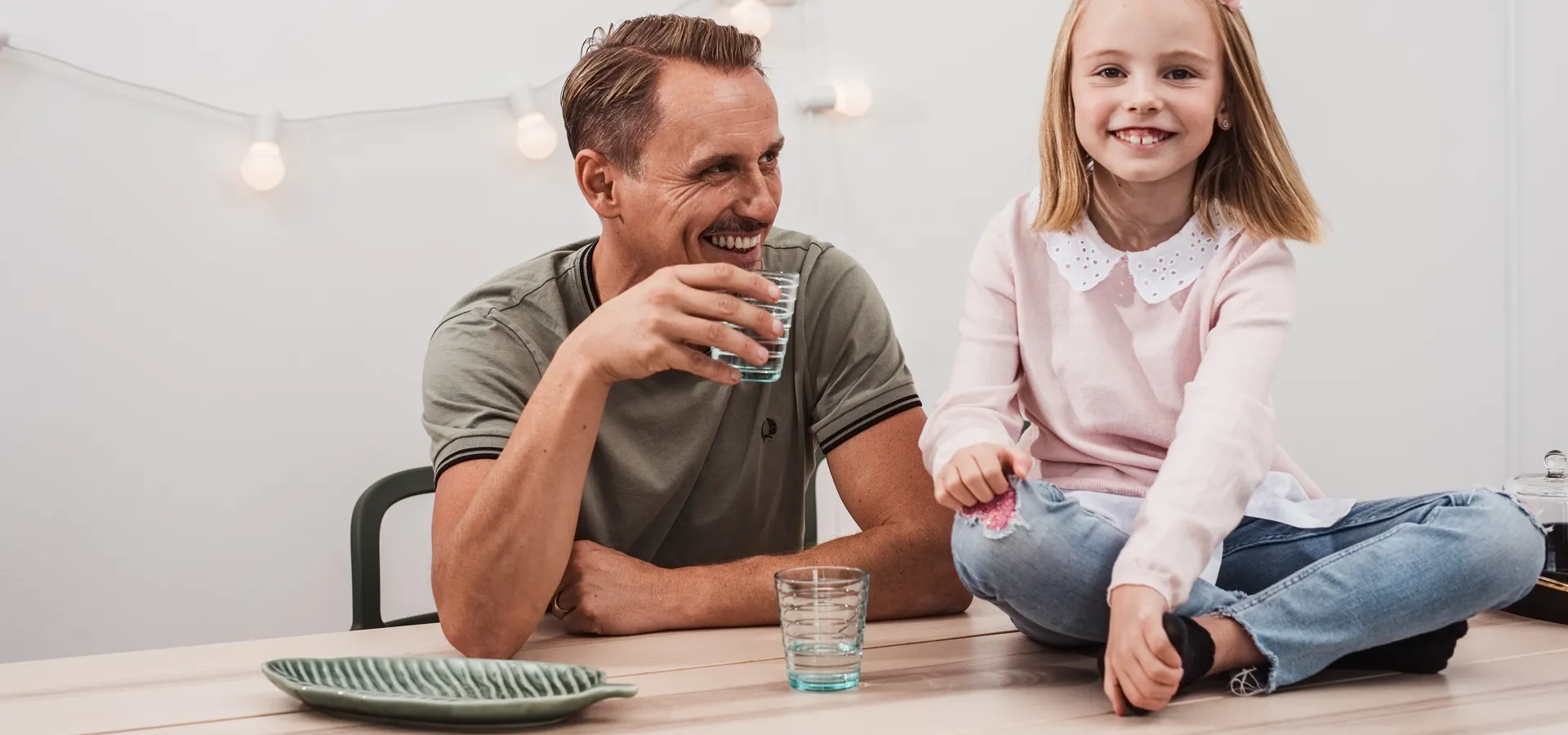 En man och en flicka i sjuårsåldern som sitter vid ett köksbord och skrattar