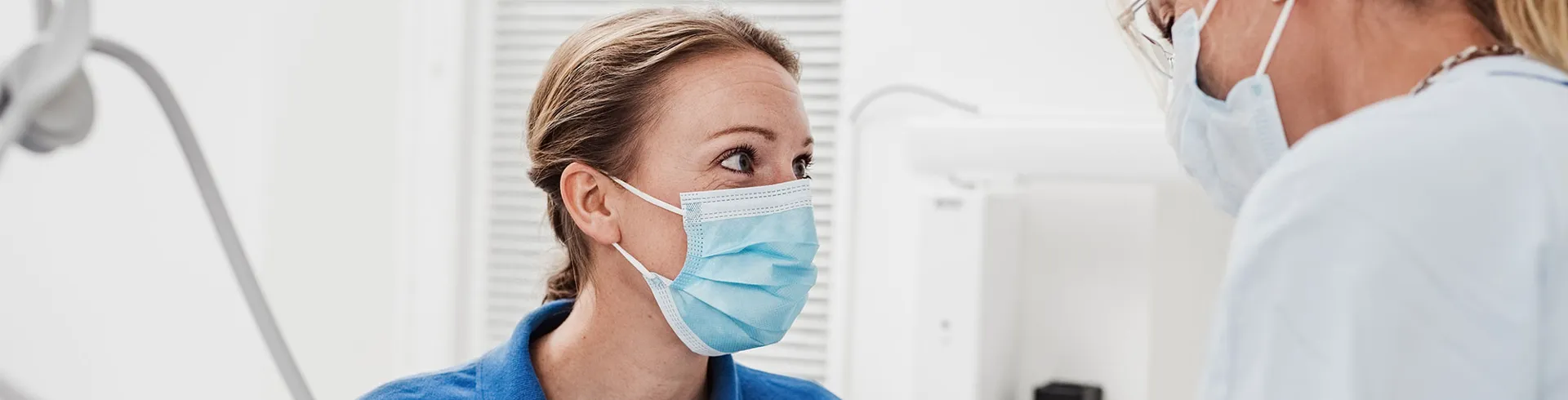 Två tandvårdsmedarbetare med munskydd tittar på varandra under ett ingrepp på en patient